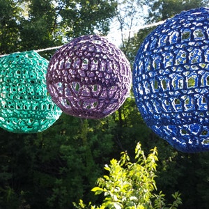 May include: Five crocheted spherical lampshades hanging from a string. The lampshades are red, teal, purple, and two shades of blue.
