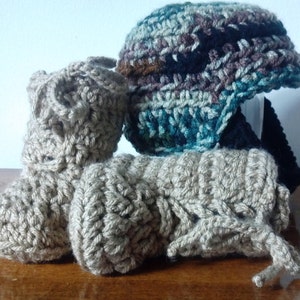 May include: A set of crocheted baby booties and a hat. The booties are beige and the hat is a mix of brown, black, and teal.
