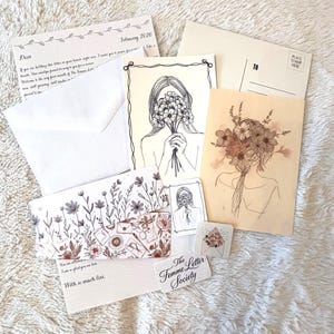 Könnte beinhalten: Eine Sammlung von Schreibwaren, darunter ein Brief vom Februar 2020, eine Postkarte mit Blumenillustration, eine kleine Karte mit einer Person, die Blumen hält, ein Lesezeichen mit Blumenmuster und ein Aufkleber mit der Aufschrift The Femme Letter Society.