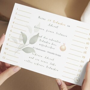 Könnte beinhalten: Ein cremefarbener, druckbarer Adventskalender mit goldenem Text und einem Aquarell-Blattdesign. Der Kalender hat 24 nummerierte Zeilen für tägliche Reflexionen, mit Text auf Deutsch. Eine goldene Ornamentgrafik ist enthalten.