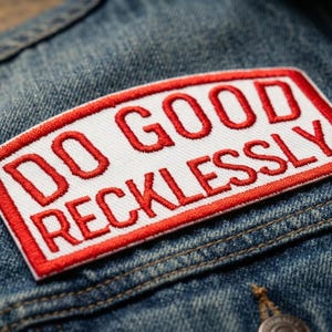 May include: Embroidered patch with the words "DO GOOD RECKLESSLY" in red on a white background, framed by a red border. The patch is affixed to a blue denim jacket, showcasing a casual, inspirational accessory.