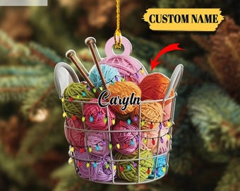 May include: A 2D flat ornament shaped like a wire basket filled with colorful yarn balls and knitting needles. The ornament is decorated with string lights and has the text "Carlyn" and "Custom Name". The top left corner has the text "2D FLAT".