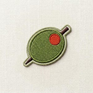 May include: Embroidered olive patch with a green oval shape, a red center, and a brown stem. The patch has a light green border and is set against a white background. This patch is perfect for adding to clothing or accessories.