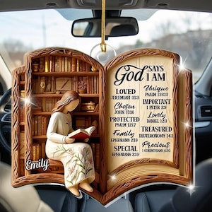 May include: A hanging car ornament shaped like an open book with a wooden frame. The left side shows a person reading in a library with the name Emily. The right side features text: God Says I Am Loved, Chosen, Protected, Family, Special, Unique, Important, Lovely, Treasured, Precious.