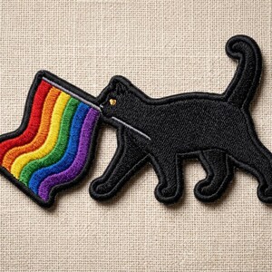 May include: Embroidered patch featuring a black cat with a rainbow-colored flag emanating from its mouth. The patch has a black border and is set against a neutral fabric background. The rainbow flag displays vibrant colors.