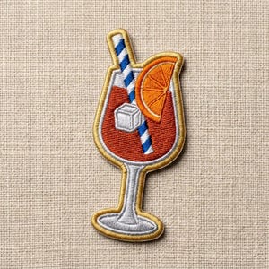 May include: Embroidered patch featuring a cocktail in a stemmed glass. The drink is a reddish-orange color, with a blue and white striped straw, an orange slice, and a single ice cube. The patch has a gold border.