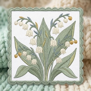 May include: A square fabric patch with a scalloped sage green border featuring an embroidered design of white lily of the valley flowers with green leaves and small yellow buds on a white background, showcasing detailed stitching throughout.