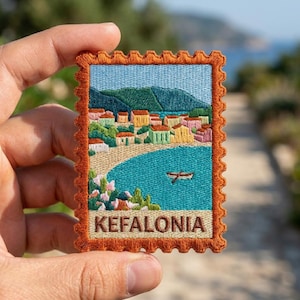 May include: A rectangular embroidered patch with a scalloped orange border, featuring a coastal landscape of Kefalonia. The design includes a turquoise sea with a small boat, a sandy beach, colorful houses, green hills, and the text KEFALONIA.