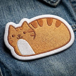 May include: Embroidered patch featuring a cartoon cat in shades of orange and brown, with a white belly and a white border. The cat is in a relaxed pose, with its eyes closed and a small smile. The patch is on a denim background.