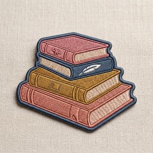 May include: Embroidered patch featuring a stack of books in shades of pink, blue, and gold. The top book has a star, the middle book has a feather, and all books have a blue border.