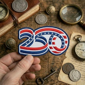 May include: An embroidered patch in the shape of the number 250, featuring a stylized ribbon design with red, white, and blue stripes and small white stars on a blue background, held up against a background of vintage coins, a book, and a pocket watch.