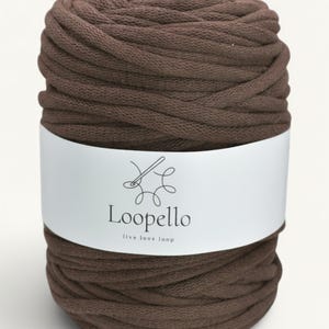 May include: A cylindrical skein of thick, dark brown yarn wrapped in a white paper label. The label features a black line drawing of a crochet hook with yarn loops and the text Loopello followed by the smaller text live love loop.
