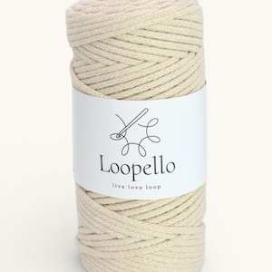 May include: A cylindrical roll of off-white macrame cord. A white label wraps around the cord, displaying the brand name "Loopello" with a needle and thread logo, and the tagline "live love loop". The cord is tightly wound.