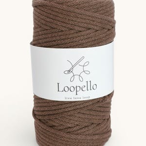 Può includere: Una bobina di cordoncino macramè marrone con un'etichetta bianca. L'etichetta presenta il marchio "Loopello" e il claim "live love loop", insieme a un logo ago e filo. Il cordoncino è ben avvolto.