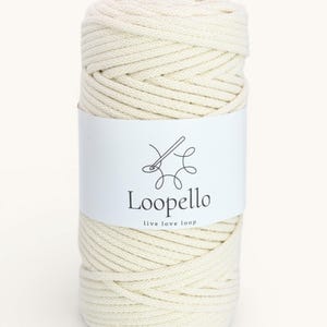 May include: A cylindrical roll of off-white macrame cord. A white label wraps around the cord, displaying the brand name "Loopello" with a needle and thread logo, and the tagline "live love loop".