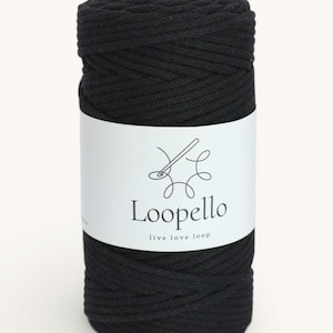 Könnte beinhalten: Eine Spule schwarzes Makramee-Garn mit einem weißen Etikett. Das Etikett zeigt ein Nadel- und Faden-Design, das Wort "Loopello" und den Slogan "live love loop". Das Garn ist fest gewickelt und bereit für Bastelprojekte.