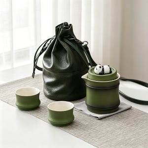 May include: A green tea set featuring a panda figurine, two cups, and a matching drawstring bag. The tea set is a dark green colour, and the cups have a bamboo-like design. The bag is made of a textured material.