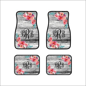 May include: Set of four car floor mats with a distressed wood grain background. Each mat features a floral design with pink and coral roses, teal accents, and a black monogram. The mats are designed for a car.