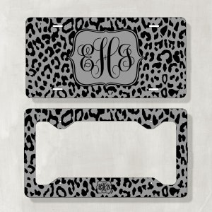 May include: A black and gray leopard print license plate frame with a monogrammed initial "EHS" in a black script font. The frame is made of metal and has a standard license plate size.