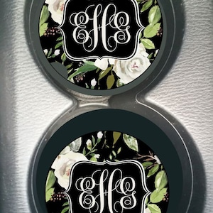 May include: Two black and white car coasters with a floral design and a monogram in the center. The monogram is "EHS".