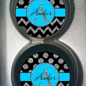 May include: Two black and silver glitter car coasters with a chevron pattern and silver glitter polka dots. The coasters have a blue stripe and a circle with the letter "A" and the name "Amber" in silver glitter.