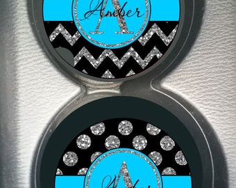 May include: Two black and silver glitter car coasters with a chevron pattern and silver glitter polka dots. The coasters have a blue stripe and a circle with the letter "A" and the name "Amber" in silver glitter.