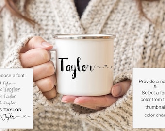 May include: White enamel mug with a black inscription that reads "Taylor" with a heart and a swirl design.  The mug is being held by a person's hand.  There are six different font options for the inscription, numbered 1 through 6.