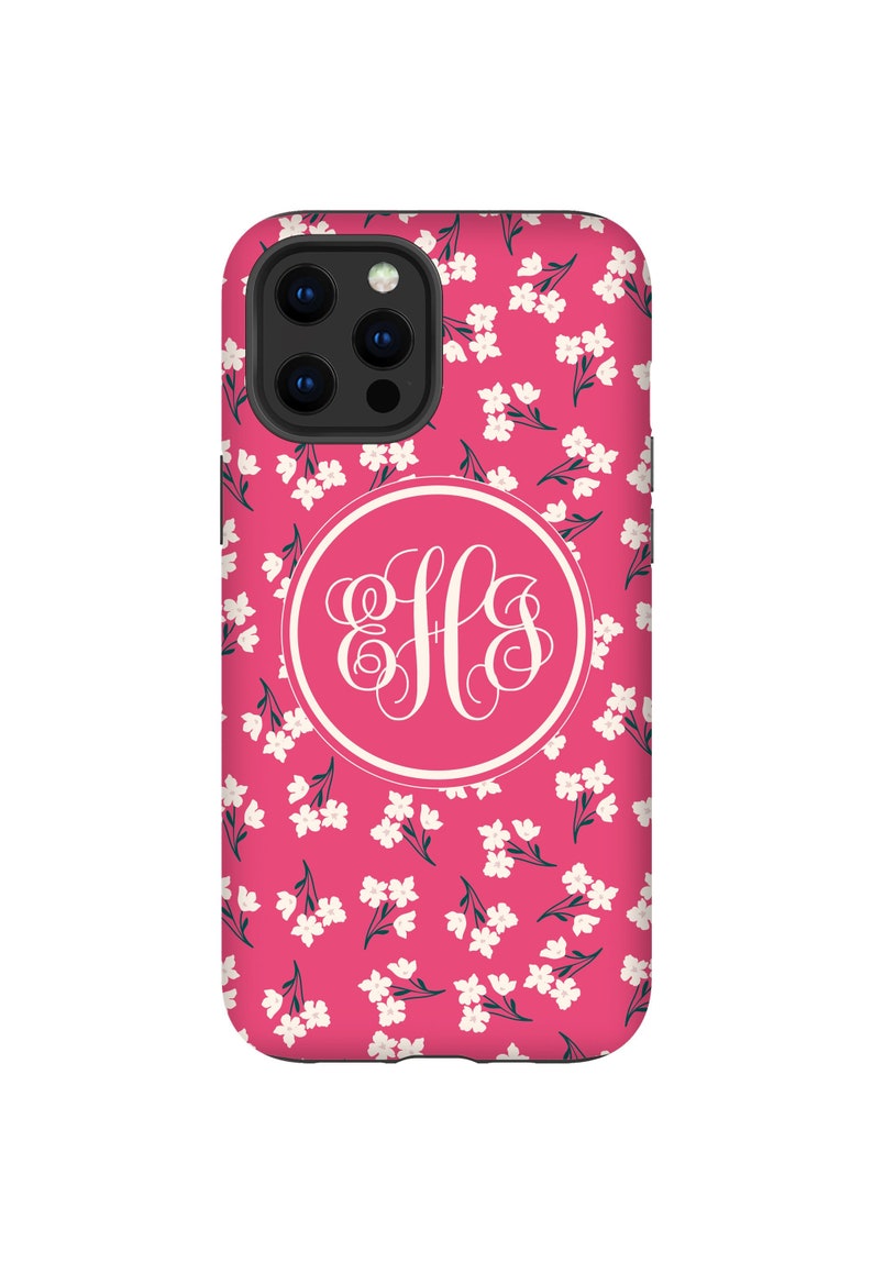 K&ouml;nnte beinhalten: Eine rosa Handyh&uuml;lle mit einem wei&szlig;en Blumenmuster und einem wei&szlig;en Monogrammkreis mit den Buchstaben "HLS" in einer Schriftart.