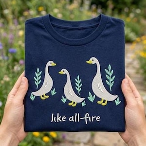 Może przedstawiać: Biały ceramiczny kubek z czarnym uchwytem i napisem "But first, coffee" w stylu odręcznym. Kubek stoi na białej powierzchni. Kubek ma około 10 cm wysokości.