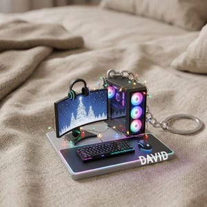 May include: Miniature gaming PC keychain with a curved monitor displaying a winter scene. Includes a keyboard, mouse, and headset. The mousepad has the name "DAVID" printed on it. The PC case is decorated with colorful lights.