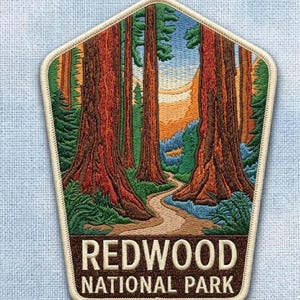 May include: Embroidered patch featuring a scenic view of Redwood National Park. The patch depicts tall redwood trees with a winding path, a blue sky, and the text "REDWOOD NATIONAL PARK" in brown letters.
