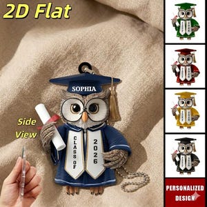 May include: A graduation owl ornament in navy blue, holding a diploma with a red ribbon. The owl wears a graduation cap with the name "SOPHIA" and a sash that reads "CLASS OF 2026". The image also shows other color variations of the owl.