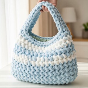May include: A hand-held, light blue and white striped, chunky knit bag. The bag has a rounded shape with a thick handle. The interior of the bag is a light green color. The bag is made of a soft, plush material.