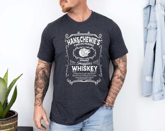 May include: Dark gray t-shirt with a white graphic that mimics a whiskey label. The text reads "Han & Chewie's Twelve Parsec Straight Smugglers Whiskey." The design includes a Millennium Falcon illustration and additional text about the whiskey's qualities.