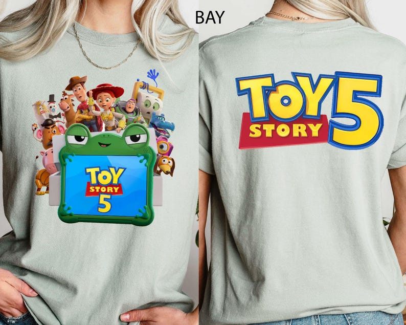 May include: A light sage green t-shirt featuring a graphic of Toy Story characters surrounding a green frog-shaped frame with the text Toy Story 5 on the front, and the text Toy Story 5 in large yellow and blue letters on the back.