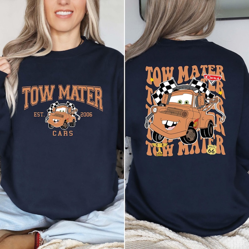 Peut inclure: Sweat-shirt bleu marine avec une image de dessin anim&eacute; de Tow Mater du film Cars. Le devant affiche le texte "Tow Mater" en orange, avec "Est. 2006" et "Cars" en dessous. Le dos r&eacute;p&egrave;te "Tow Mater" avec une r&eacute;f&eacute;rence &agrave; la Route 66.
