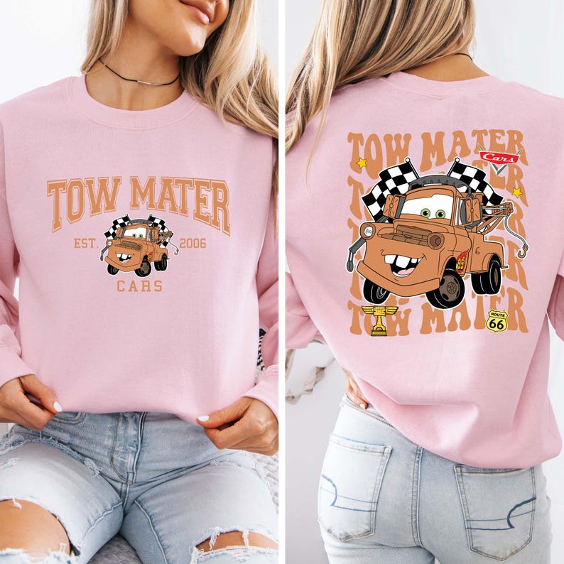 Peut inclure: Sweat-shirt rose clair avec une image de dessin anim&eacute; de Martin de Cars. Le devant affiche "Tow Mater" au-dessus de l'image, avec "Est. 2006" et "Cars" en dessous. Le dos pr&eacute;sente une image plus grande de Martin.