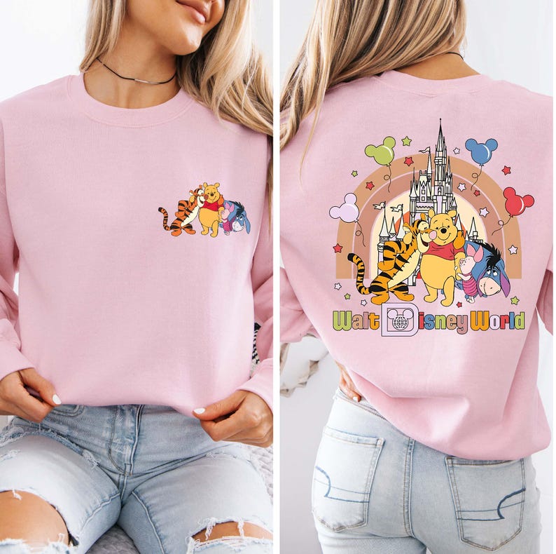 Op de afbeelding: Een lichtroze sweatshirt met een cartoonafbeelding van Winnie de Poeh, Teigetje en Iejoor. De voorkant heeft de karakters samen, en de achterkant heeft de karakters met een regenboog, kasteel en de tekst "Walt Disney World".