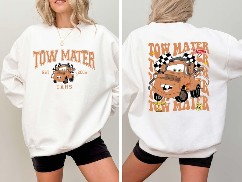 Peut inclure: Sweat-shirt blanc avec une image de dessin anim&eacute; de Martin la d&eacute;panneuse du film Cars. Le design avant comprend le texte "TOW MATER EST. 2006 CARS". Le design arri&egrave;re montre Martin avec des drapeaux &agrave; damiers.