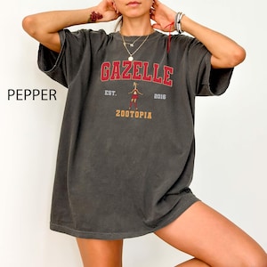 May include: Pepper-colored oversized t-shirt with the word "GAZELLE" in red block letters above a cartoon figure and the text "ZOOTOPIA". The shirt also features the text "EST. 2016".