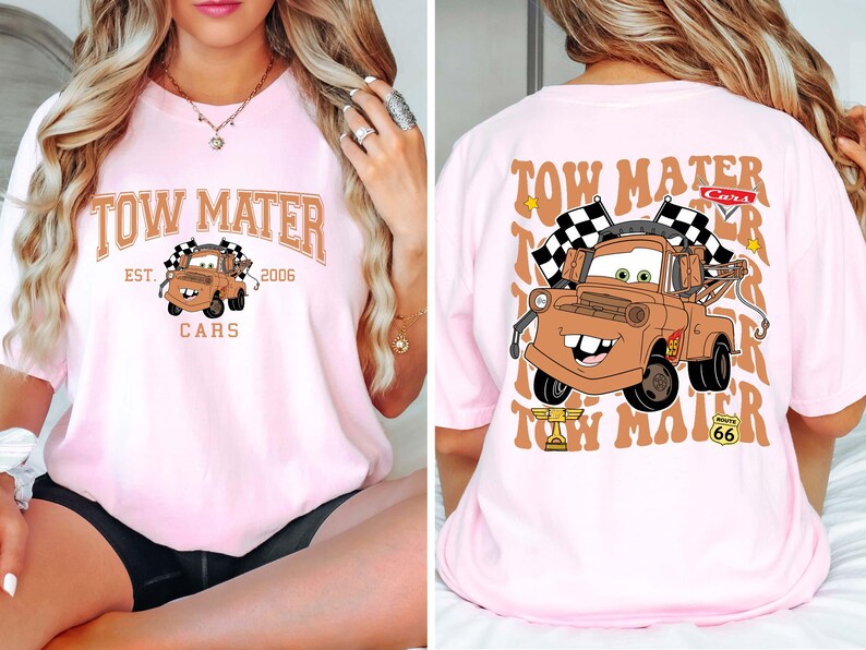 Puede incluir: Camiseta rosa claro con una imagen de dibujos animados de Mate de la pel&iacute;cula Cars. La parte delantera muestra "Tow Mater Cars Est. 2006". La parte trasera muestra una imagen m&aacute;s grande de Mate con banderas a cuadros y el texto "Tow Mater".