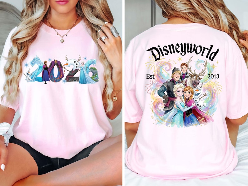 K&ouml;nnte beinhalten: Hellrosa T-Shirt mit der Aufschrift "2026" und Frozen-Figuren. Auf der R&uuml;ckseite steht "Disneyworld Est 2013" mit einer farbenfrohen Grafik der Charaktere. Ein lustiges Design f&uuml;r Disney-Fans.