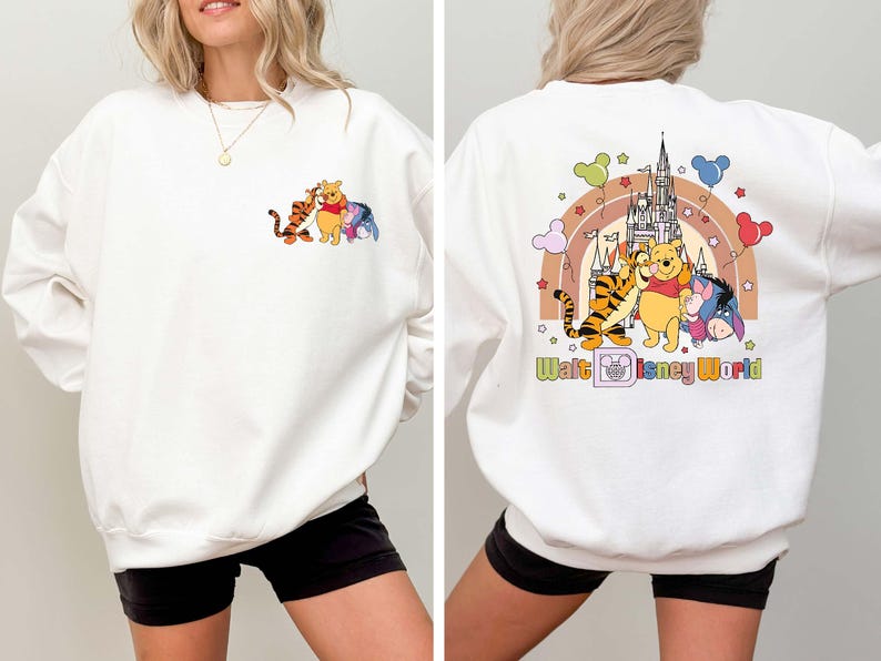 Op de afbeelding: Witte sweatshirt met een kleurrijke afbeelding van Winnie de Poeh, Teigetje, Iejoor en een kasteel. De voorkant heeft de karakters en de achterkant heeft de karakters, een regenboog en de tekst "Walt Disney World".