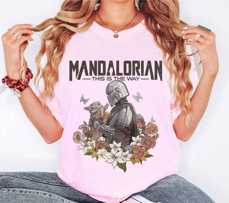 May include: Pink t-shirt featuring a graphic of The Mandalorian and Grogu surrounded by flowers and butterflies. The text "MANDALORIAN - THIS IS THE WAY" is printed across the top.