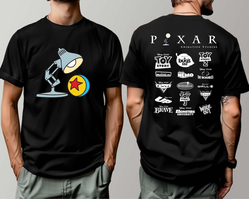 May include: Black t-shirt featuring a cartoon illustration of the Pixar lamp and ball on the front. The back of the shirt displays the Pixar Animation Studios logo and logos from various Pixar films, including Toy Story, Finding Nemo, and Monsters University.