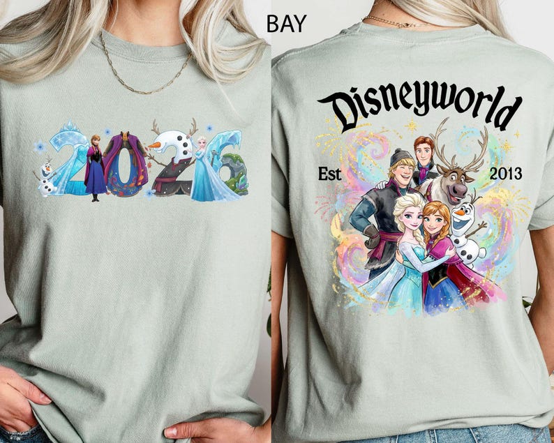 K&ouml;nnte beinhalten: Hellgr&uuml;nes T-Shirt mit farbenfroher Grafik von Frozen-Charakteren und dem Jahr 2026. Auf der R&uuml;ckseite des Shirts steht der Text "Disneyworld Est 2013" mit einer Gruppe von Charakteren.