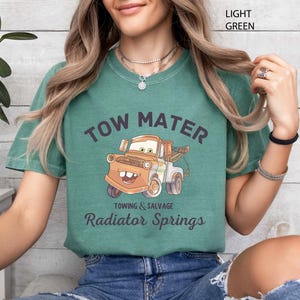 Peut inclure: T-shirt vert clair avec une image de dessin anim&eacute; de Martin de Cars. Le texte "TOW MATER" est au-dessus du personnage, avec "Towing & Salvage" et "Radiator Springs" en dessous. Le t-shirt est de style d&eacute;contract&eacute; et confortable.