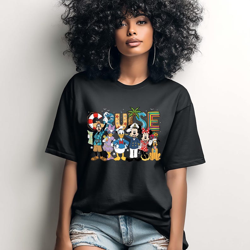 May include: Black t-shirt featuring the word "CRUISE" in colorful letters with a palm tree graphic. The shirt also displays cartoon characters including Mickey Mouse, Minnie Mouse, Donald Duck, and Goofy. The shirt is worn by a person.