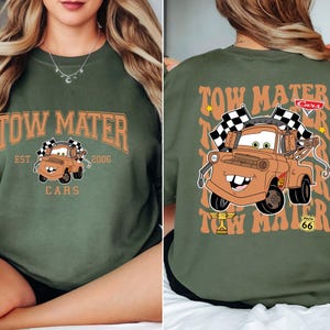 Peut inclure: Un sweat-shirt vert olive avec un motif de Martin de Cars. Le devant affiche le texte "Tow Mater" au-dessus d'une image du personnage, avec "Est. 2006" et "Cars" en dessous. Le dos r&eacute;p&egrave;te le texte et le personnage.