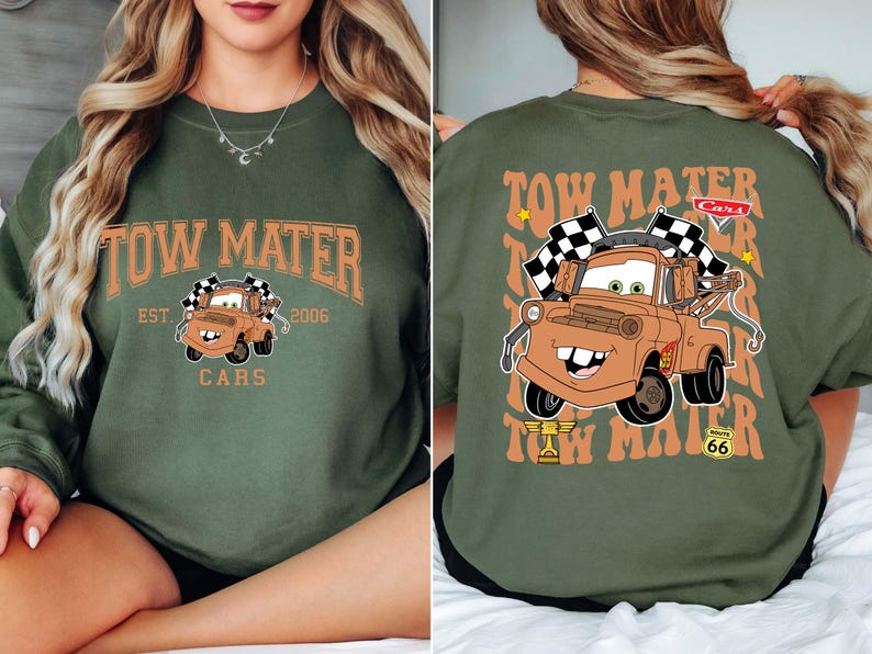 Peut inclure: Un sweat-shirt vert olive avec un motif de Martin de Cars. Le devant affiche le texte "Tow Mater" au-dessus d'une image du personnage, avec "Est. 2006" et "Cars" en dessous. Le dos r&eacute;p&egrave;te le texte et le personnage.